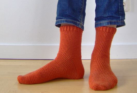 Virkade, orange strumpor på fötter med ben klädda i jeans